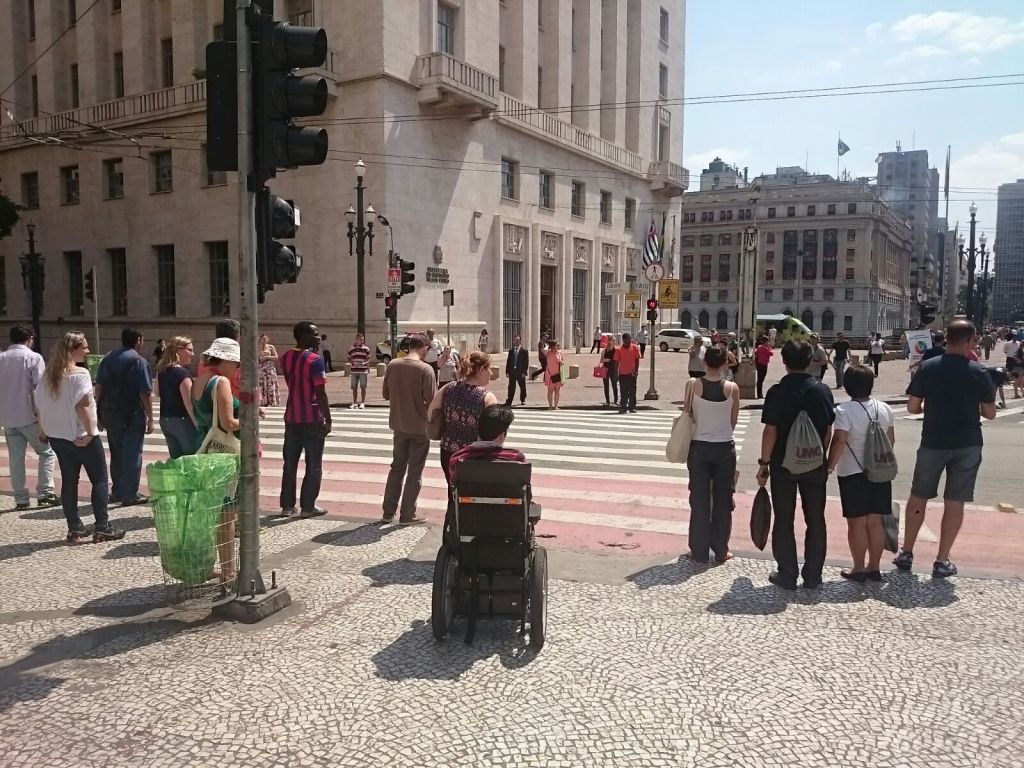 Pessoas, uma delas em cadeira de rodas, esperam para atravessar no centro de São Paulo