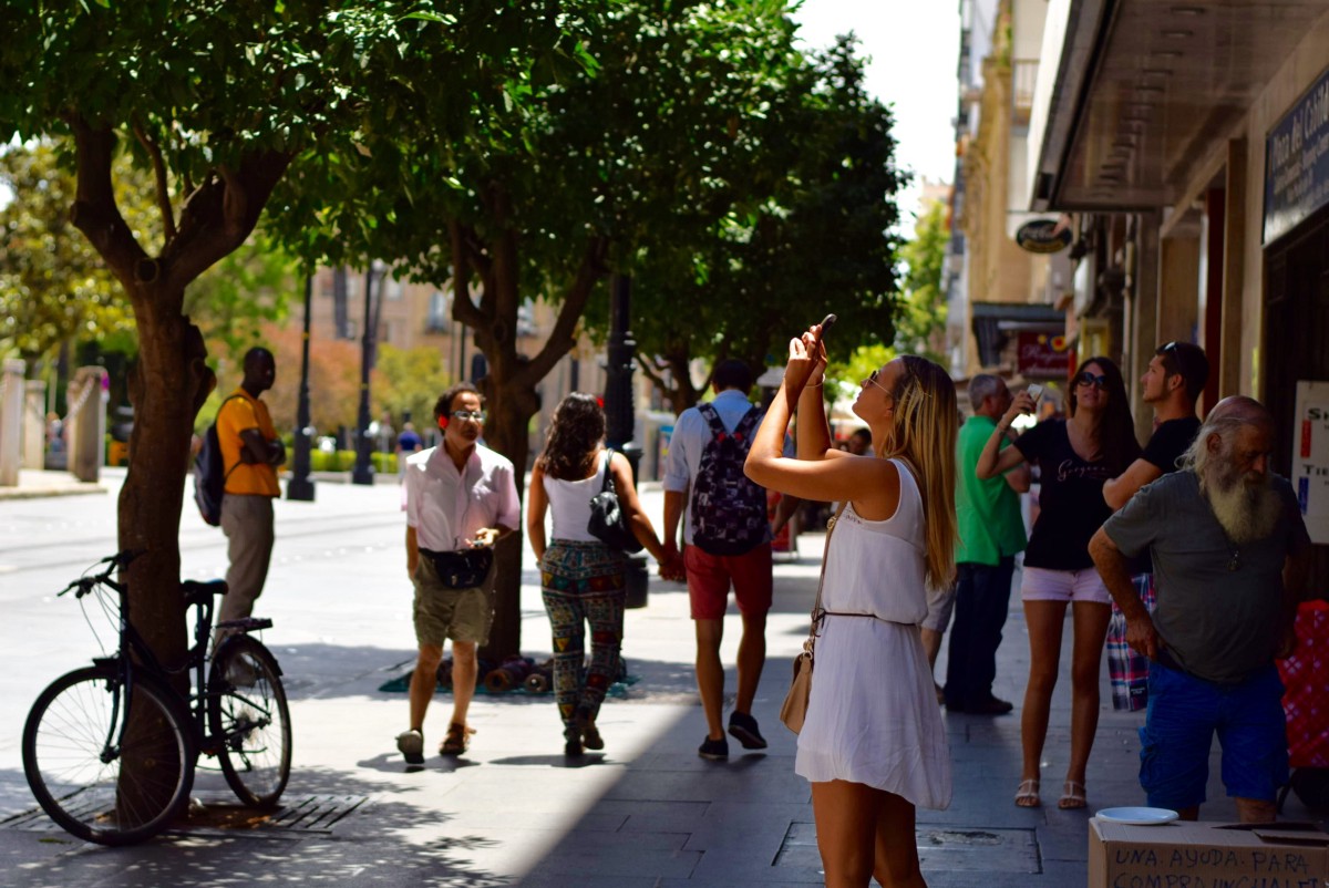 Pedestres caminham numa calçada arborizada com uma bicicleta estacionada