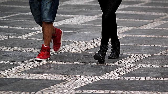 Pés de duas pessoas caminhando sobre calçada de mosaico português