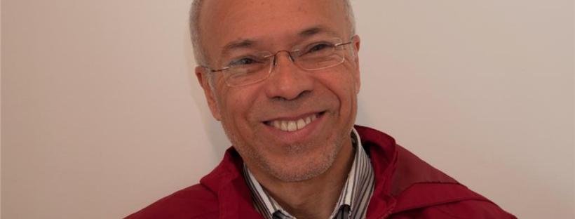Retrato de Marcos de Sousa, sorrindo, de óculos e jaqueta vermelha