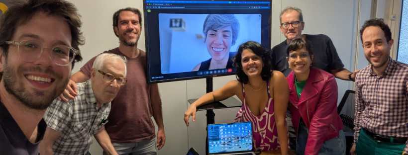 Participantes da Assembleia Geral Extraordinária posam em uma sala de reunião, com outra participante na videochamada