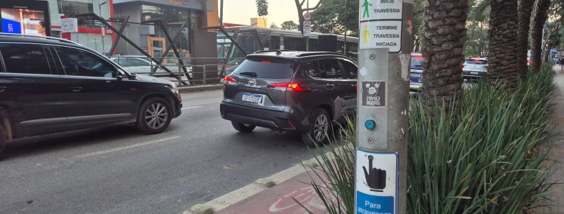 Poste com botoeira para pedestres ao lado de uma via com carros, em São Paulo